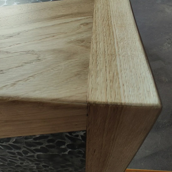 tavolo in quercia, superficie in rovere massello sagomata in pannelli geometrici, con inserti a triangoli di resina traslucida a effetto ciottolato. Linee pulite e volumi decisi definiscono un’estetica contemporanea.